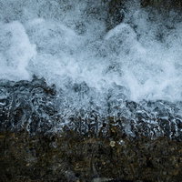 岩場に勢いよく流れ込む水と白い水飛沫が激しく舞う渓流の写真