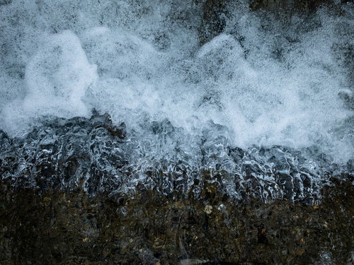 岩場に勢いよく流れ込む水と白い水飛沫が激しく舞う渓流