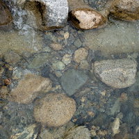 透明に澄んだ水の河原で見える川底の石と岩の写真
