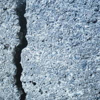 縦方向に走るクラックが入ったグレーのブロック壁の写真