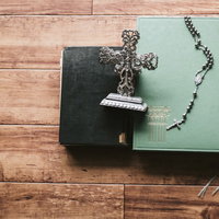 木製テーブルに置かれた聖書とロザリオと燭台の写真