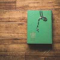 緑色の表紙の古書の上に置かれたロザリオと十字架の写真