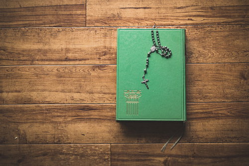 緑色の表紙の古書の上に置かれたロザリオと十字架