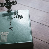 聖書の上に置かれた黒いロザリオと十字架、木製テーブルの写真