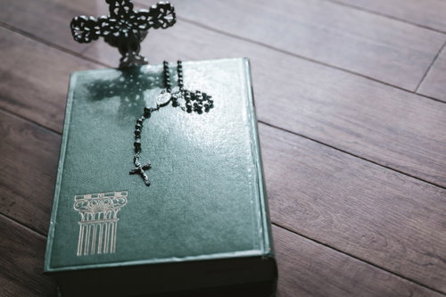 聖書の上に置かれた黒いロザリオと十字架、木製テーブル