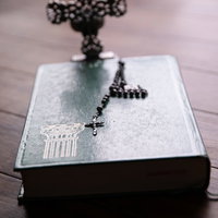 窓際に置かれた聖書の上の黒いロザリオと十字架の写真