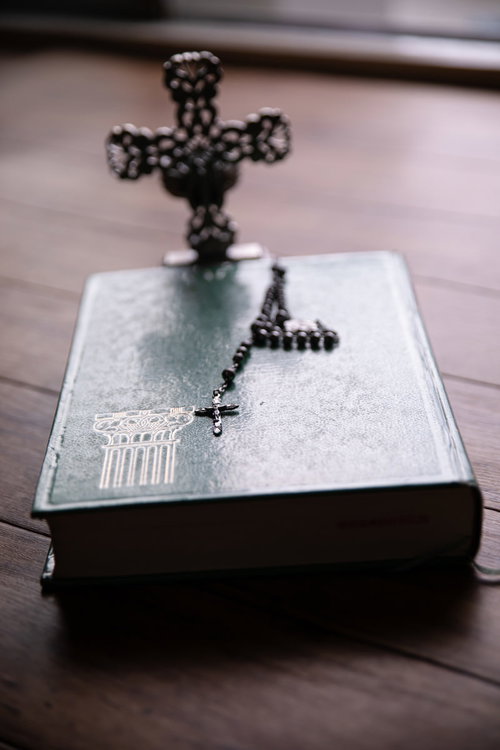 窓際に置かれた聖書の上の黒いロザリオと十字架