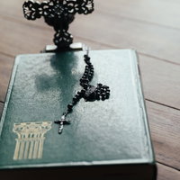 聖書の上に置かれた黒い十字架のロザリオのチャームの写真