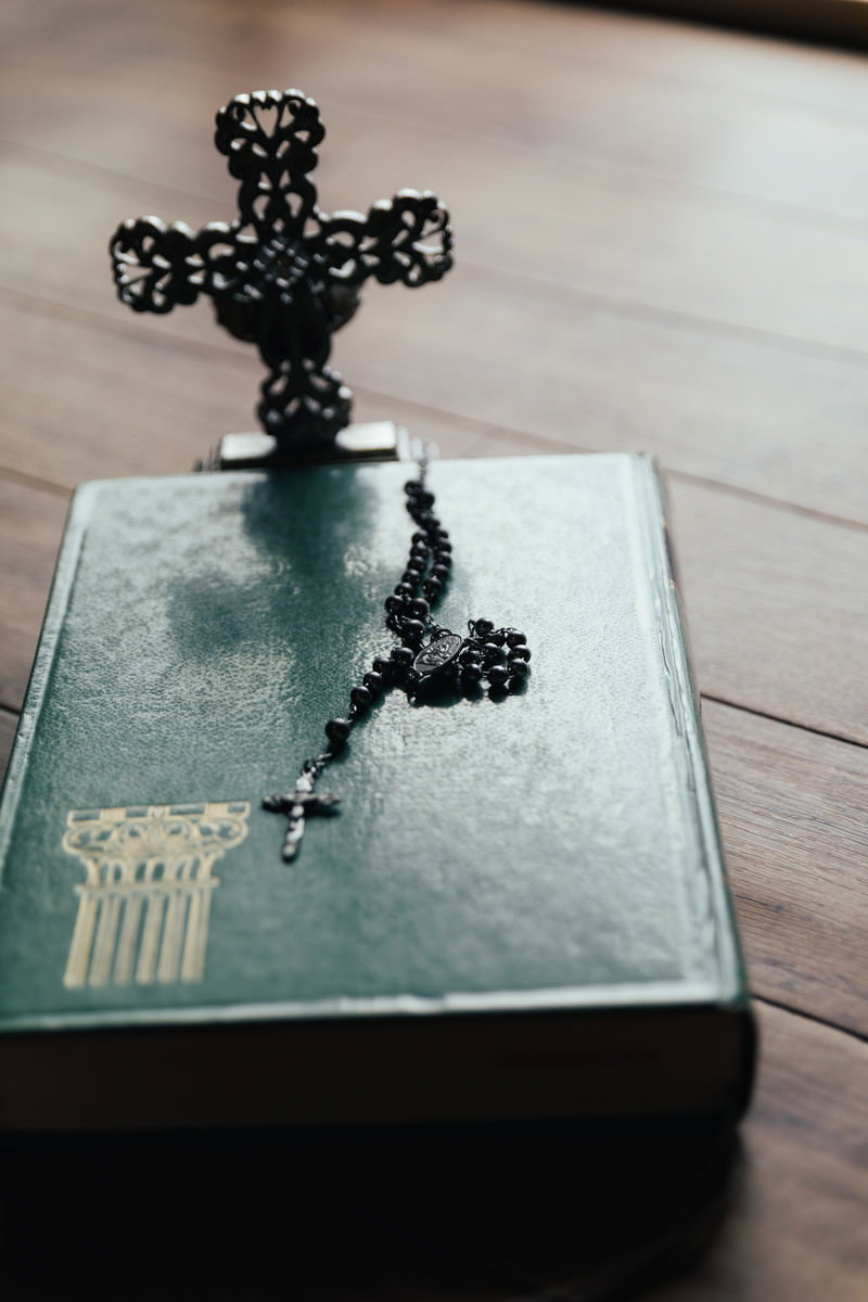 緑色の聖書の上に黒い十字架のロザリオが置かれている