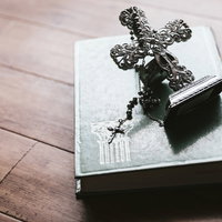 十字架の燭台とロザリオが置かれた古書と聖書の宗教用品の写真