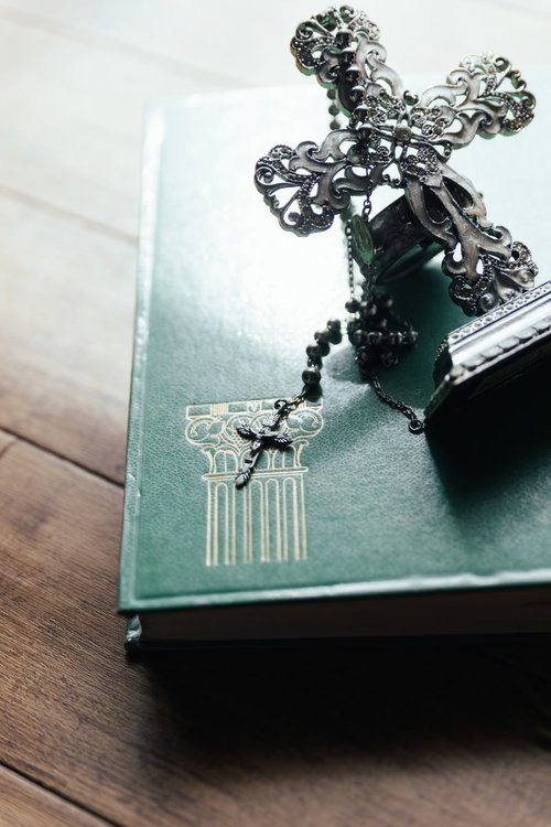 自然光が差し込む中のロザリオと十字架の燭台、古書