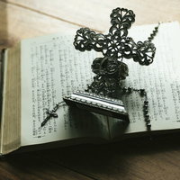 窓辺に置かれた古書の上の十字架の燭台とロザリオの写真