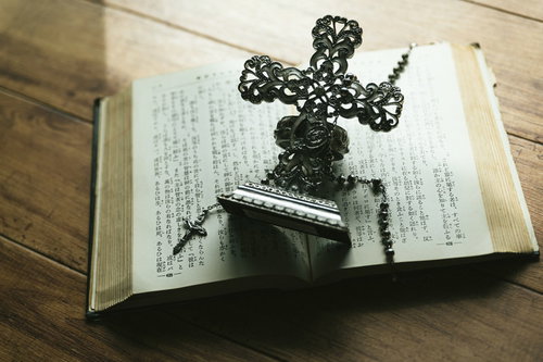 窓辺に置かれた古書の上の十字架の燭台とロザリオ