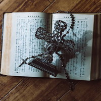 聖書の上に置かれた金属製の十字架の燭台とロザリオの写真