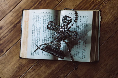 聖書の上に置かれた金属製の十字架の燭台とロザリオ