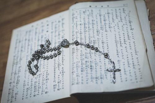 聖書のページの上に置かれた十字架付きロザリオと古書