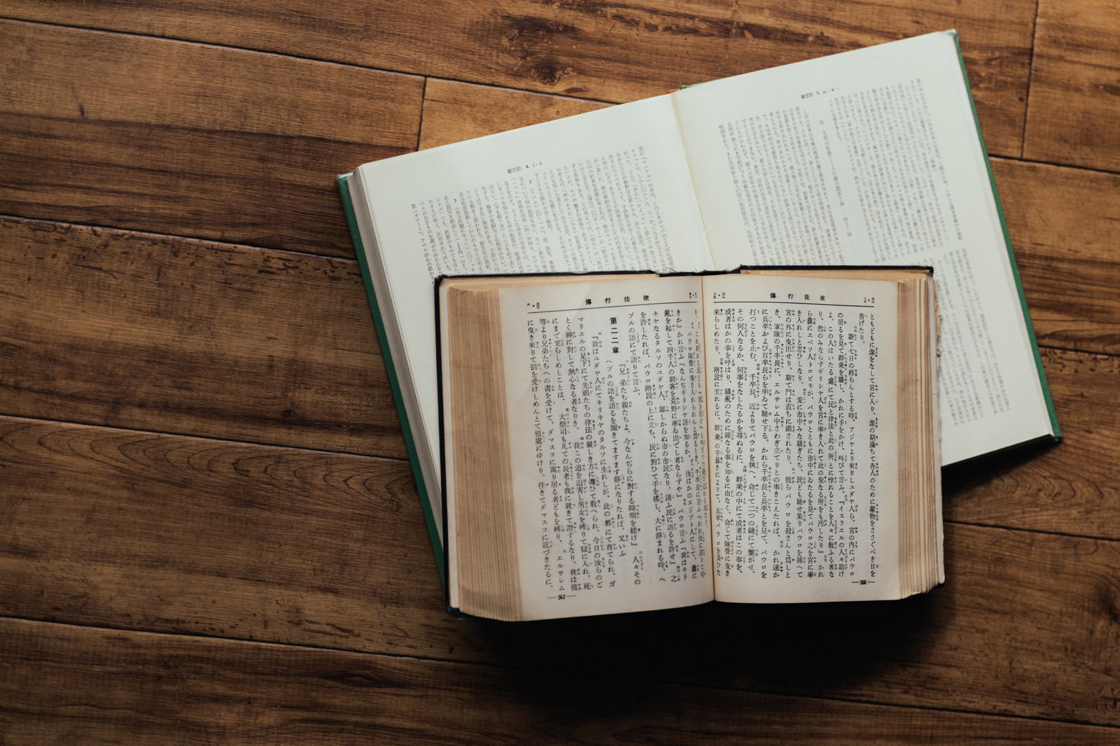 木製テーブルの上に開かれた聖書と閉じられた古書が重ねて置かれている