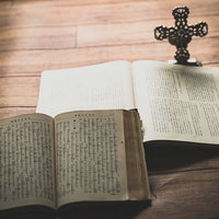 窓際に置かれた開かれた聖書と十字架の燭台の写真