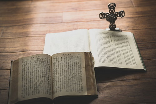 窓際に置かれた開かれた聖書と十字架の燭台