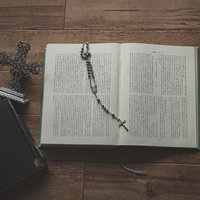 開いた聖書の上に置かれたロザリオと十字架の写真