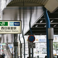 JR西日暮里駅の緑と青の駅名看板と駅前の街並み風景の写真