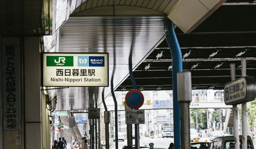JR西日暮里駅の緑と青の駅名看板と駅前の街並み風景