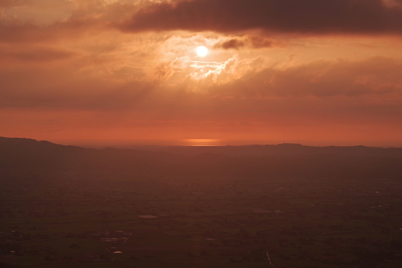 夕暮れの空で雲間から差し込む太陽の光と山々のシルエット