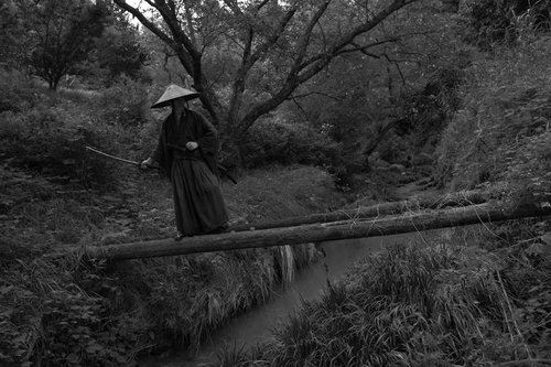 モノクロで撮影した丸太橋の先で待ち構える追手