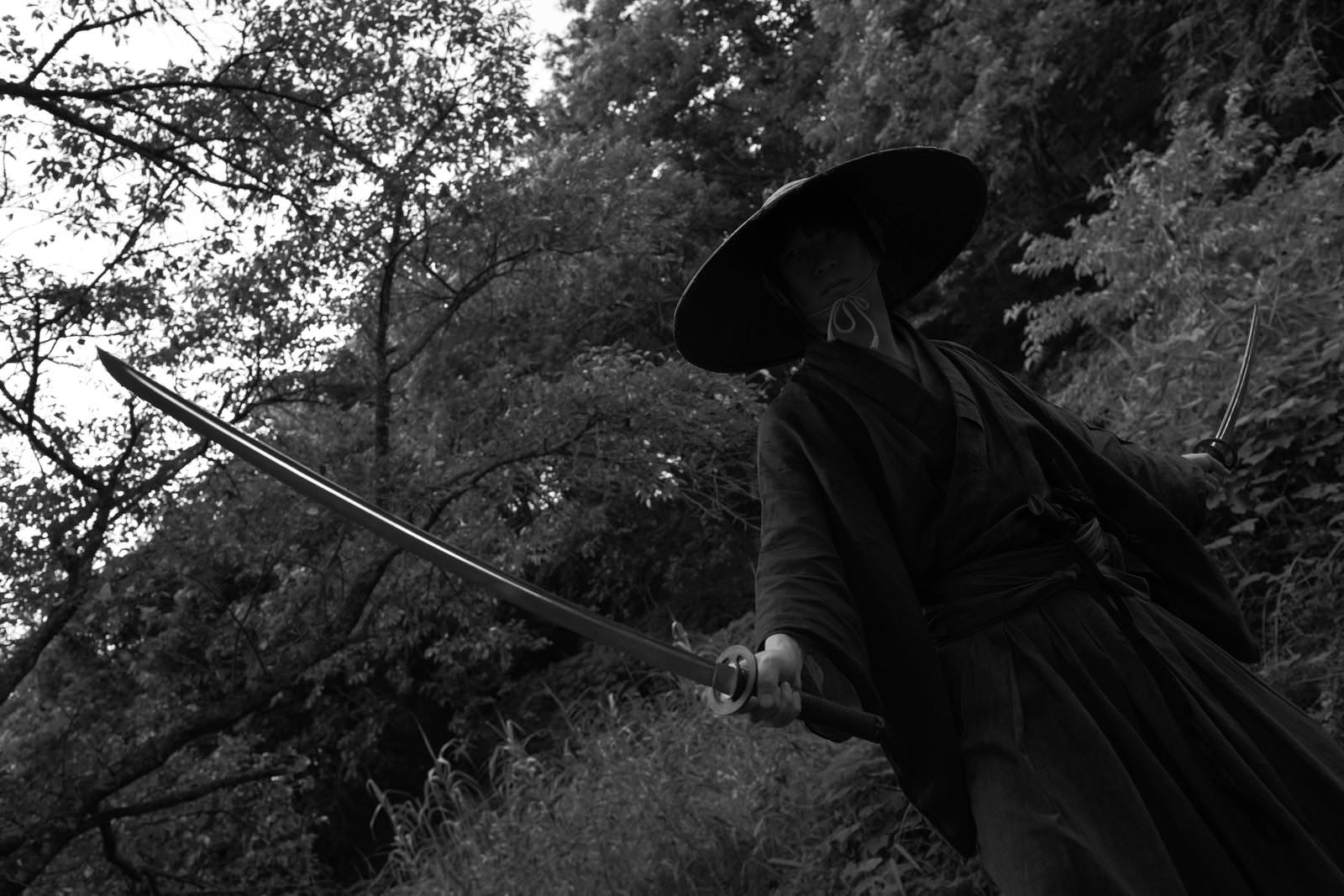 樹木を背景に刀を構える黒い着物の男性用心棒［モデル：まーこ］