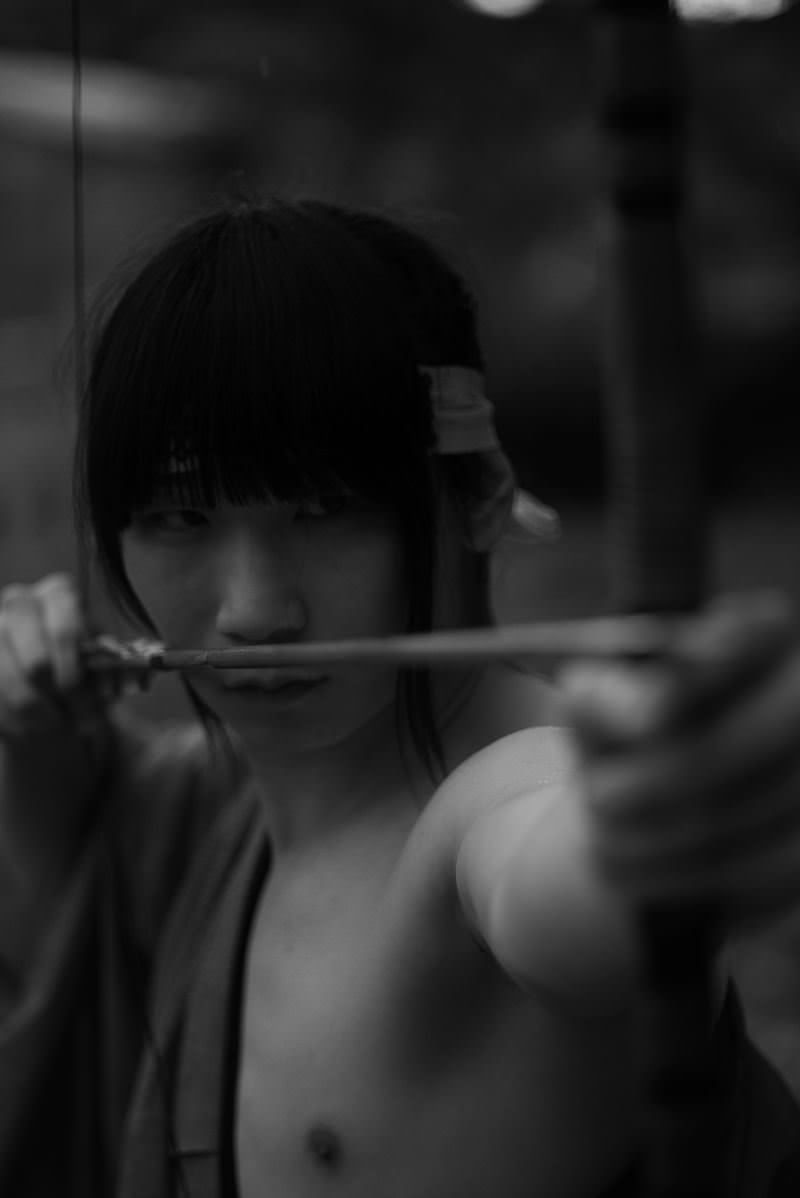 弓に矢をつがえて正面を狙う袴姿の人物を捉えたモノクロ写真［モデル：まーこ］