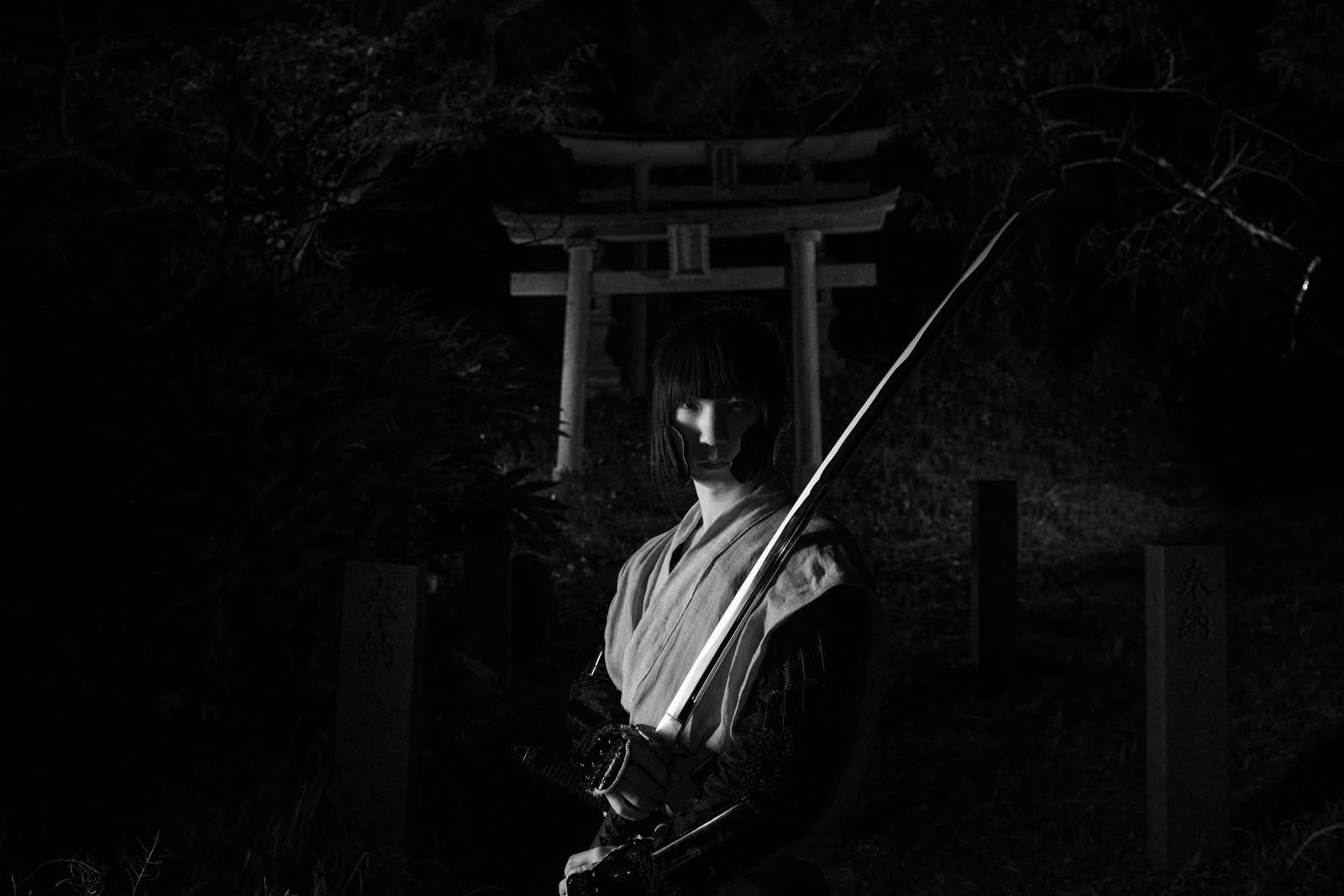 暗闇の中、神社の鳥居の前で袴を着た男性が日本刀を構えている［モデル：まーこ］