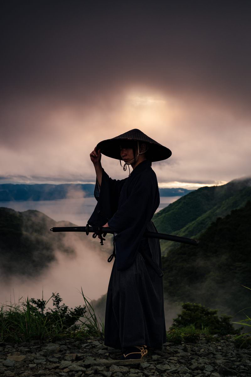 夕暮れの山間で網代笠に手を添えて振り返る袴姿の侍［モデル：まーこ］