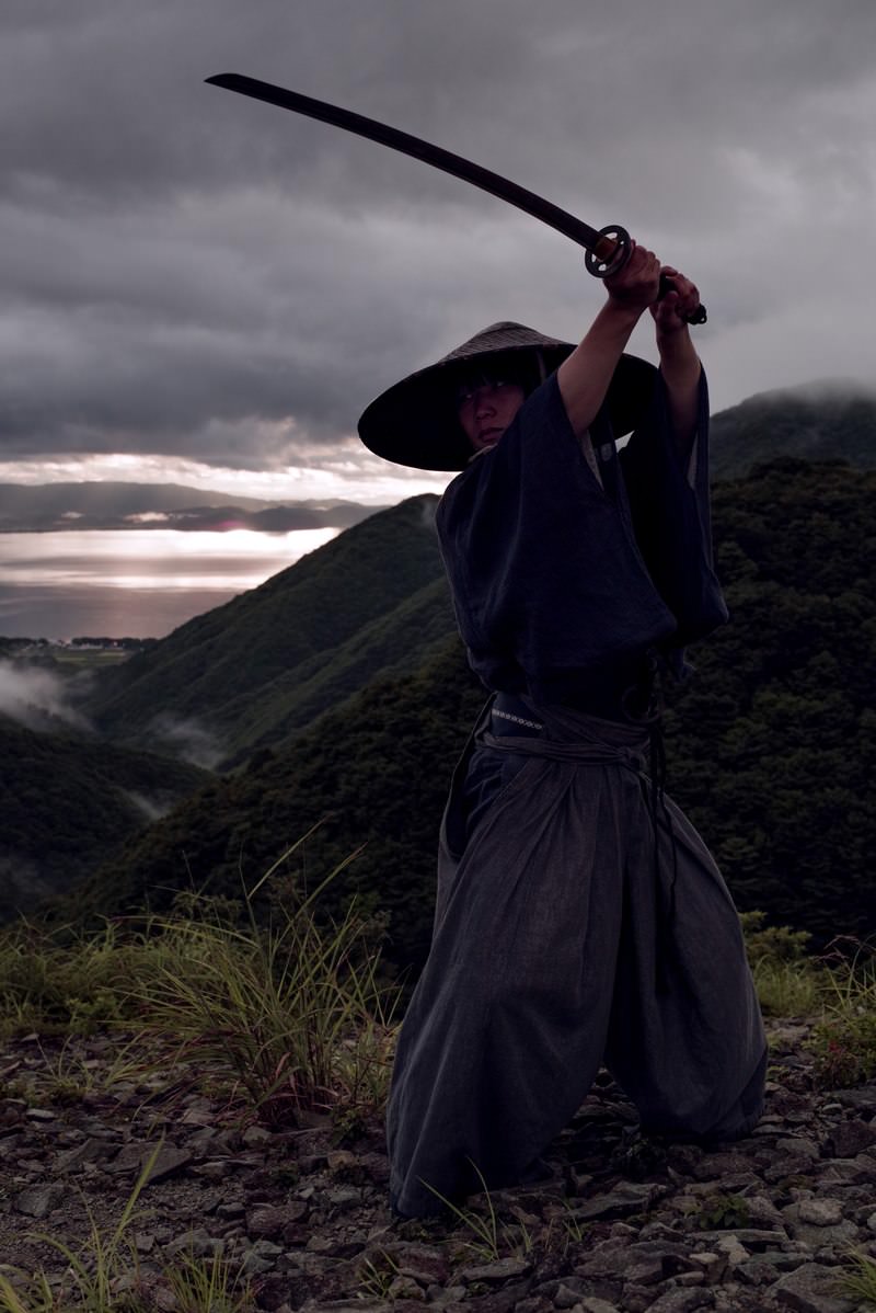 薄暗い登山道で刀を構える黒い袴姿の侍［モデル：まーこ］