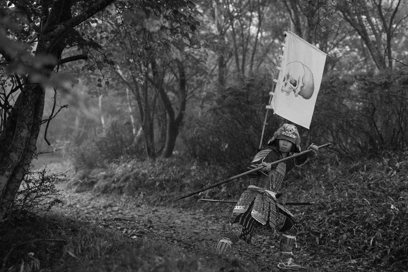 黒い甲冑を身に着けて槍を構える武士の白黒写真［モデル：まーこ］