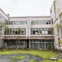 廃墟と化した小学校の中庭と校舎、窓ガラス破損と外壁剥落の写真