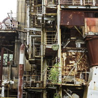 崩れそうな工場廃墟の錆びた鉄骨と配管が複雑に絡み合うの写真