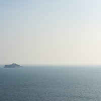 海の向こうに水平線上に浮かぶ軍艦島の廃墟の写真