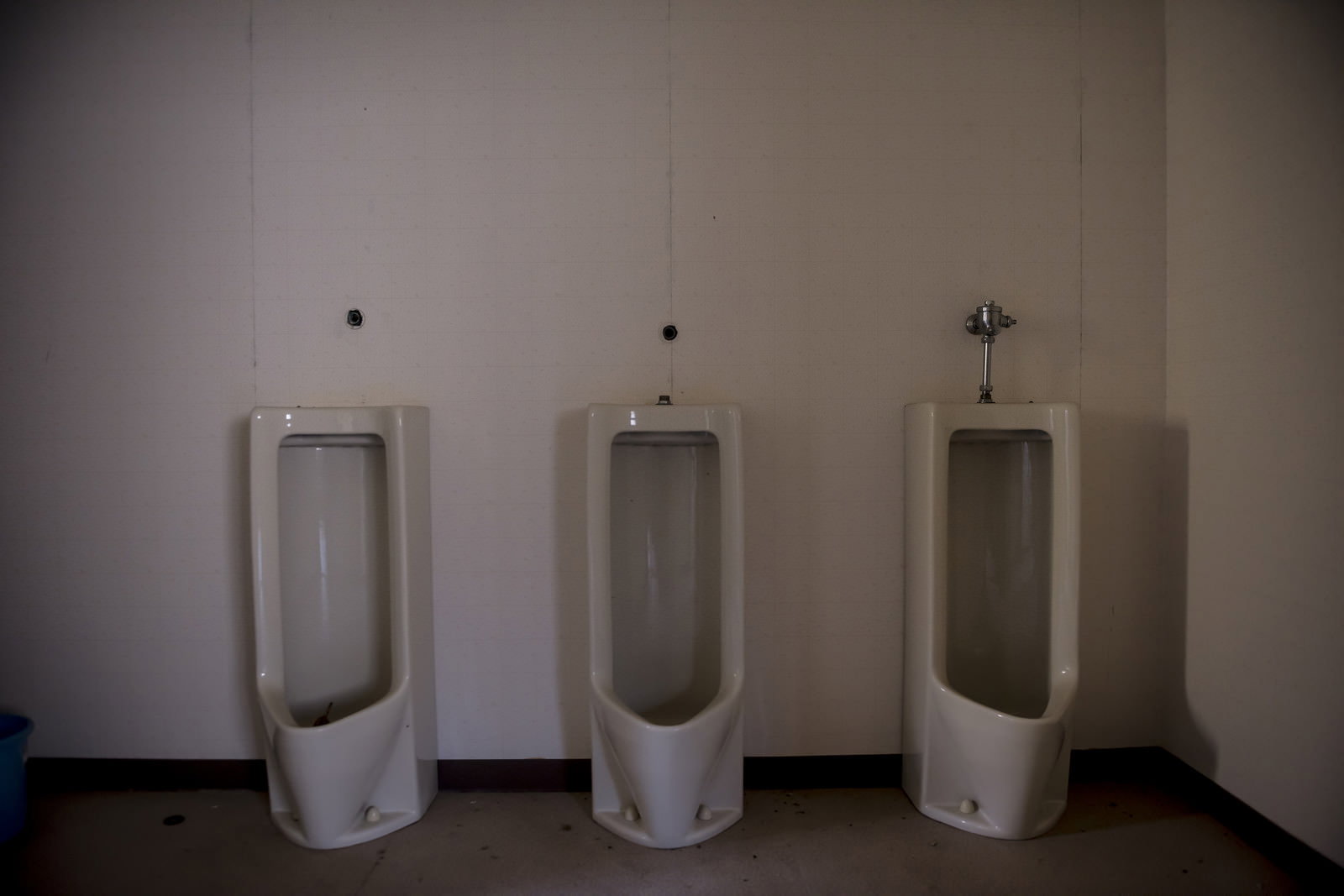 薄暗い廃墟のトイレに3台の白い小便器が並ぶ