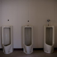 使われていない不気味な廃墟のトイレ、薄暗い空間に並ぶ白い小便器の写真