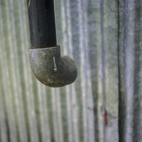 古いトタン壁に取り付けられた黒い排水管と経年劣化の写真