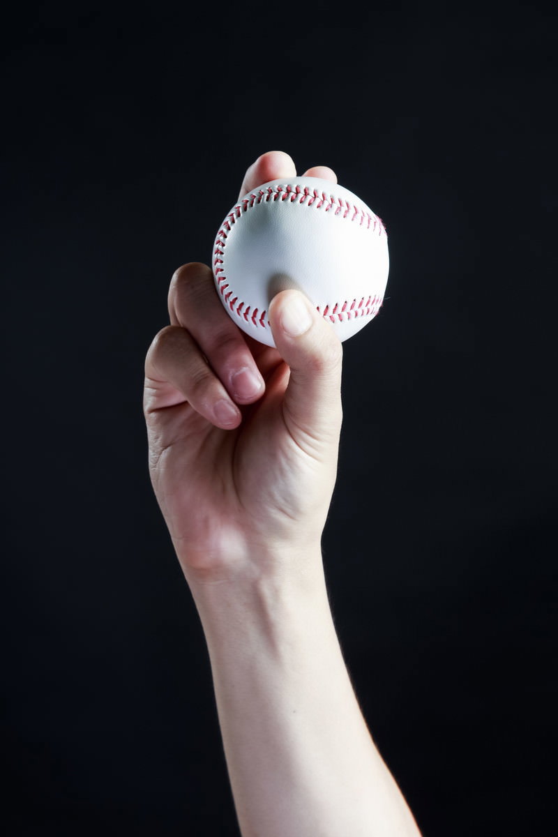 黒い背景で野球ボールを持ちカーブの握り方を示している手