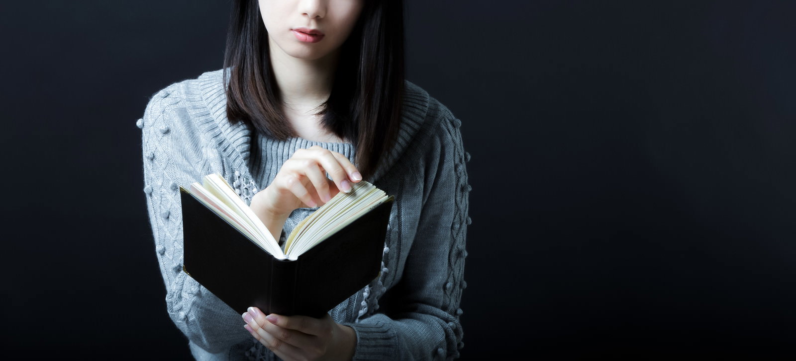 グレーのニットを着た女性が本を読む