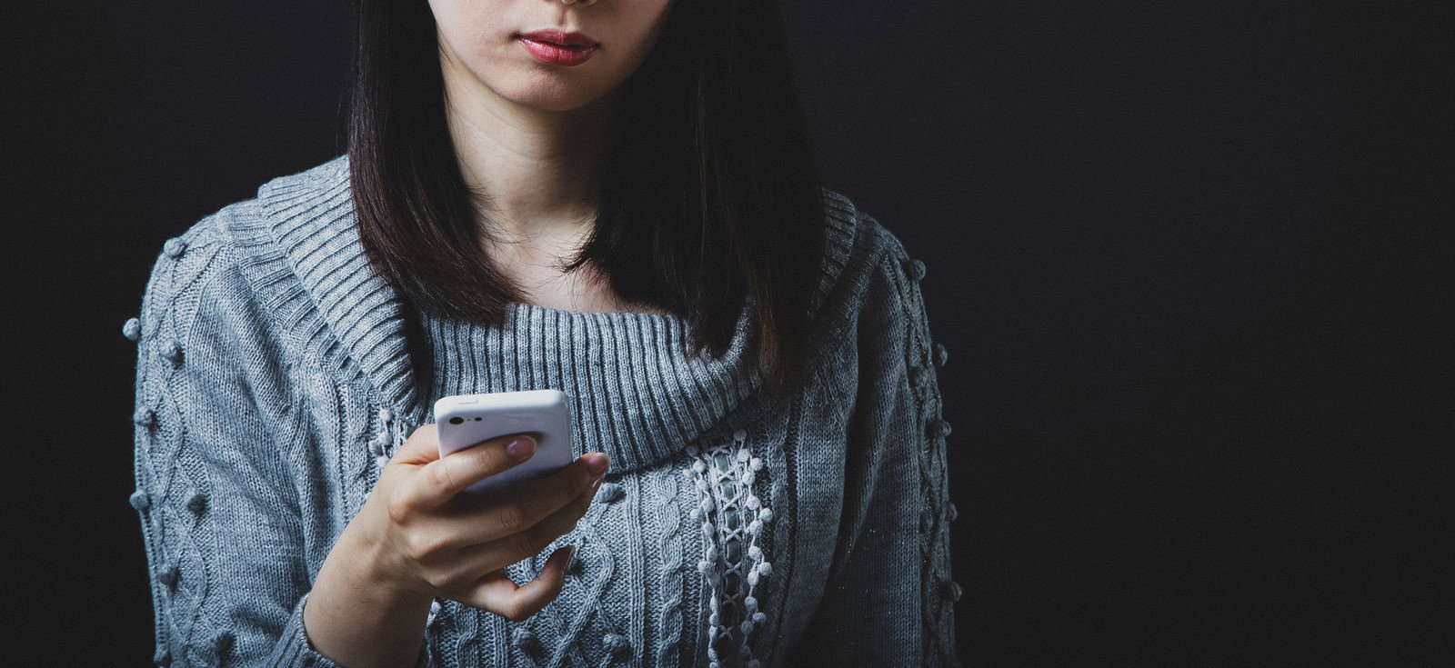 グレーのニットを着た女性がスマートフォンを見て困惑している様子