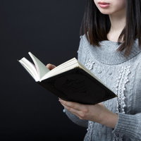 暗闇の中で本を読む女性の手元の写真