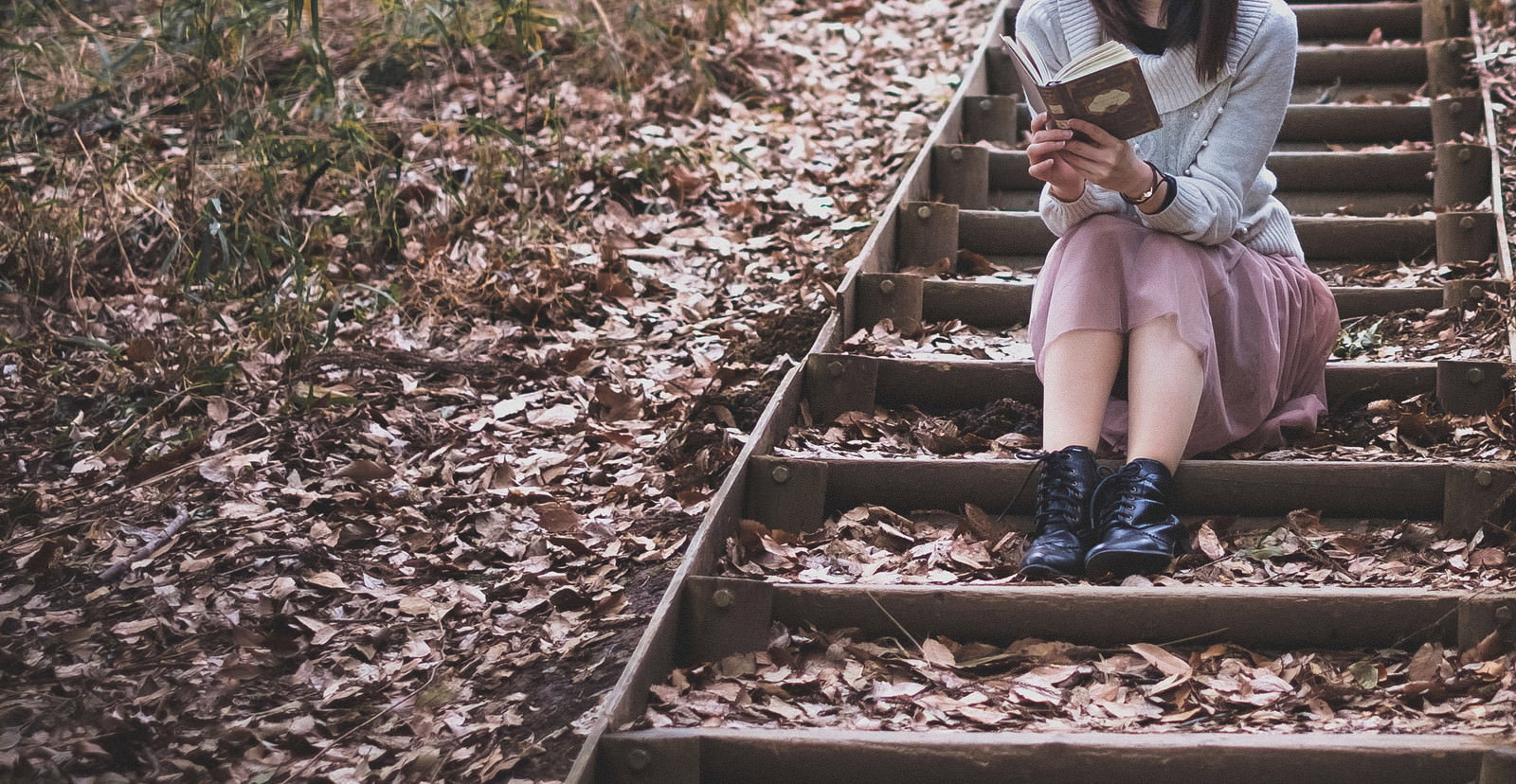落ち葉が積もった階段に座って本を読んでいる女性