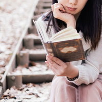 石の階段で洋書を読む白いニットの女性の読書風景の写真
