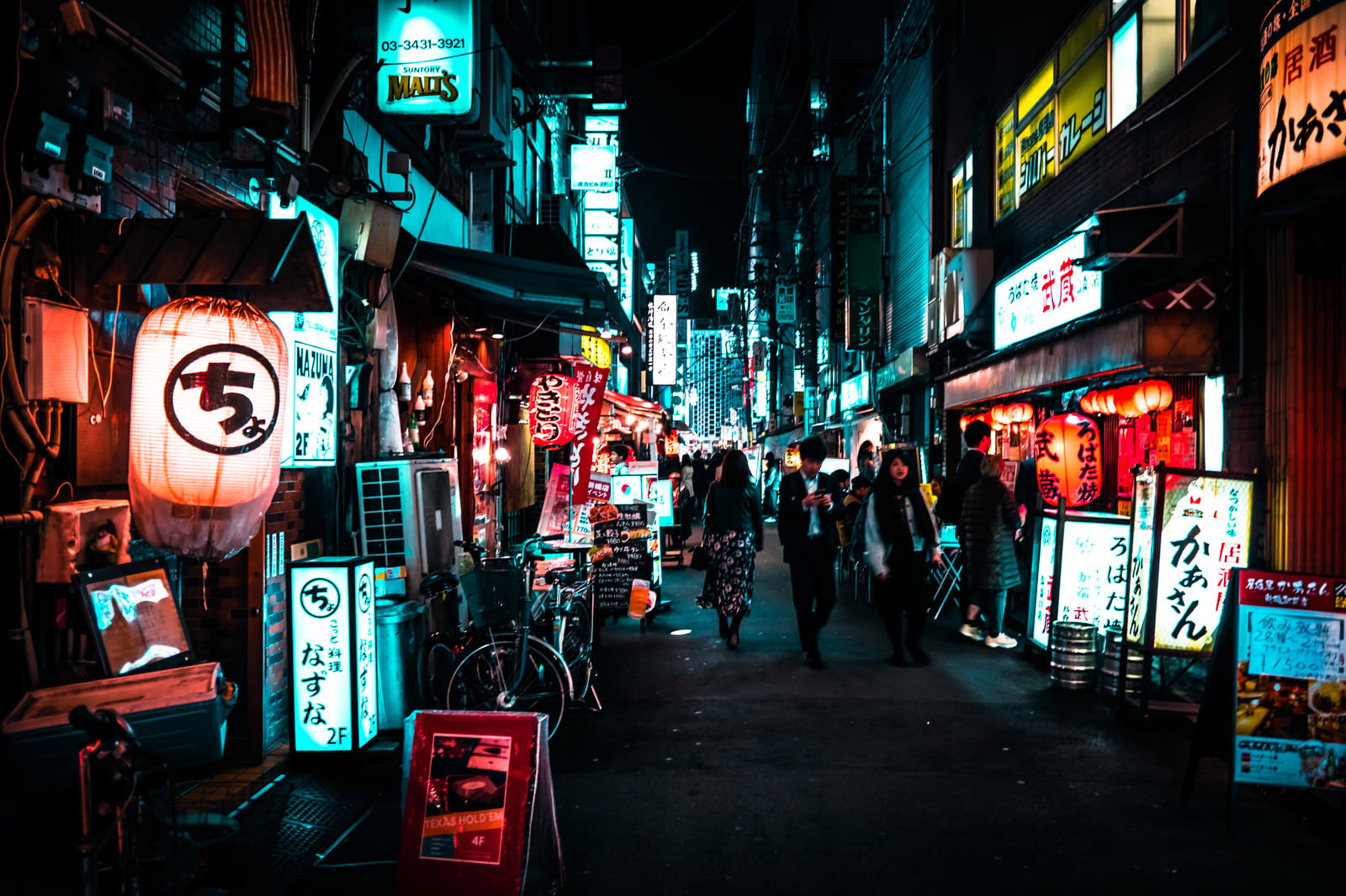 ネオン看板が並ぶ夜の飲み屋街を歩く人々