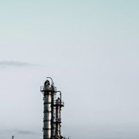 空を大きく占める曇り空に高い金属製の塔と横向きの筒がある工場設備の写真