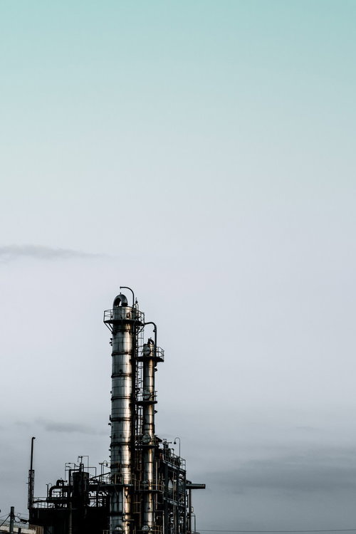 空を大きく占める曇り空に高い金属製の塔と横向きの筒がある工場設備