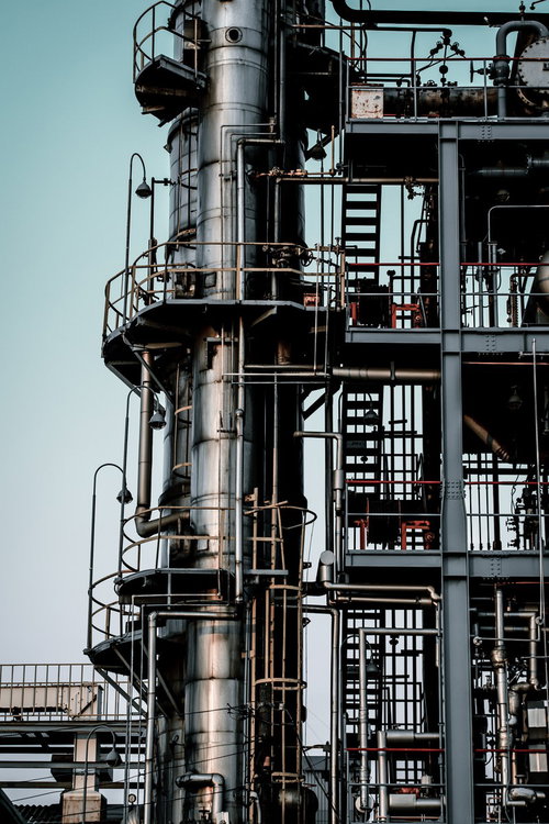 銀色の太い円柱タンクと多層の金属製階段や配管が組む工場設備